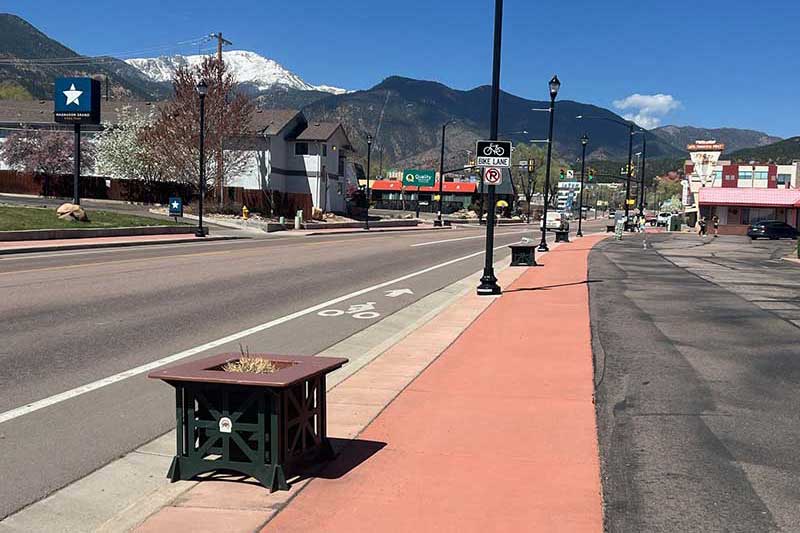 This photo shows the streetscape along the avenue with Pikes Peak in the background against a blue sky. Manitou Springs Urban Renewal Authority Success Stories. This photo shows the streetscape along the avenue with Pikes Peak in the background against a blue sky. Manitou Springs Urban Renewal Authority Success Stories.