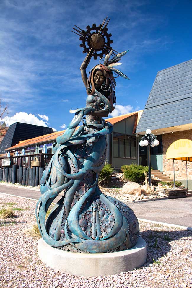 This photo shows the Spirit of Manitou sculpture by artist Jodi Bliss in front of the Quality Inn. Success Stories from the Manitou Springs Urban Renewal Authority. This photo shows the Spirit of Manitou sculpture by artist Jodi Bliss in front of the Quality Inn. Success Stories from the Manitou Springs Urban Renewal Authority.