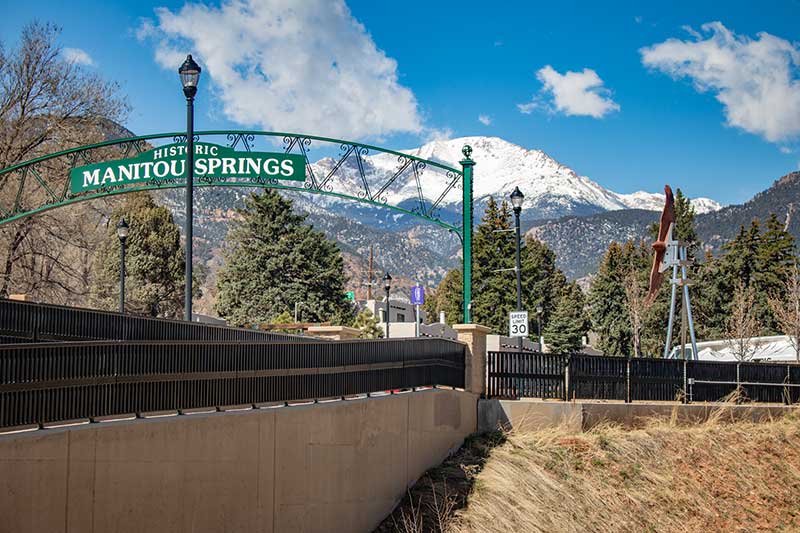 Image showing the Historic Manitou Springs Arch against a blue sky, which is seen as you enter the Gateway to Manitou Springs. Manitou Springs Urban Renewal Authority. Image showing the Historic Manitou Springs Arch against a blue sky, which is seen as you enter the Gateway to Manitou Springs. Manitou Springs Urban Renewal Authority.